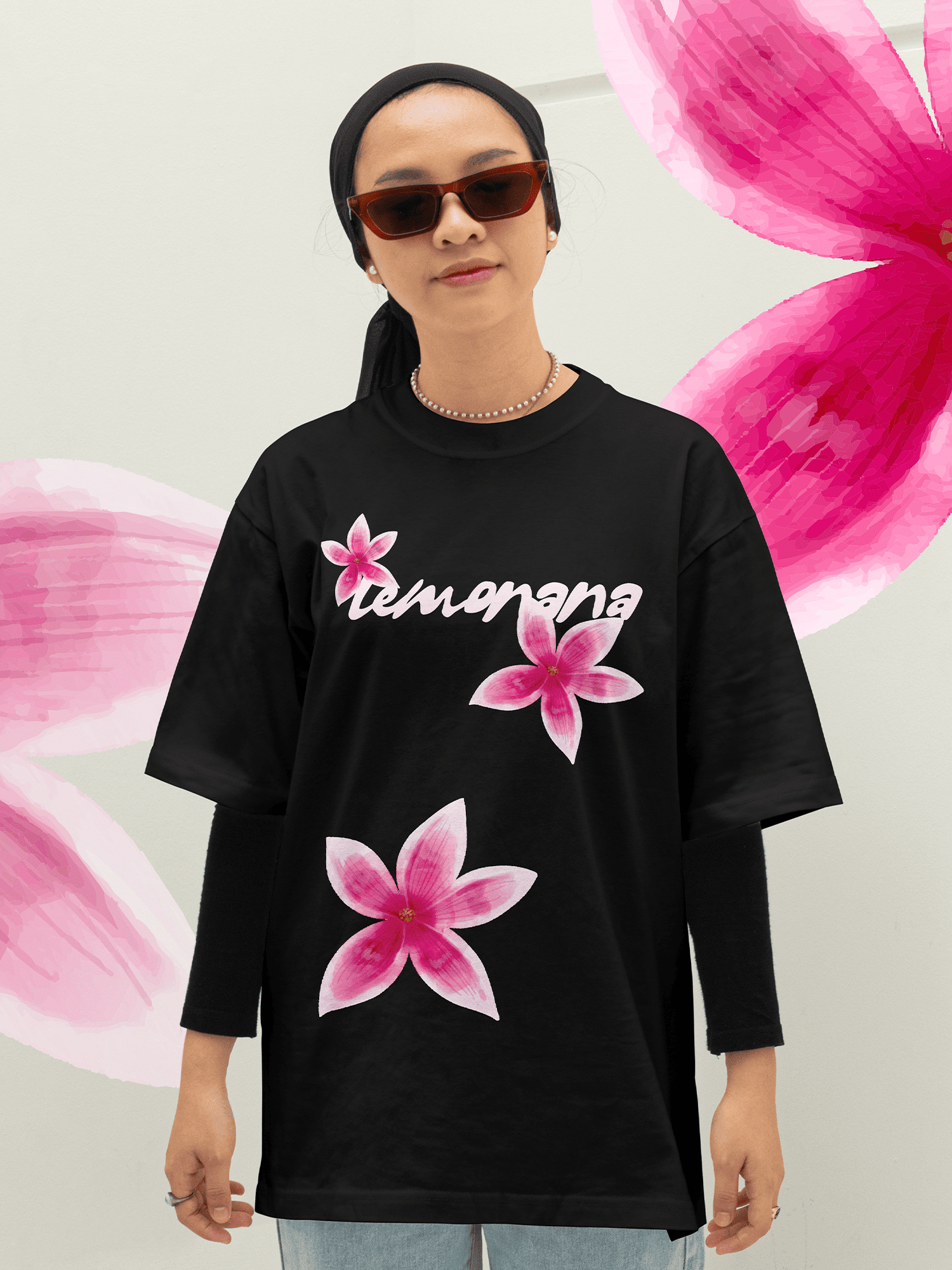 Person wearing a black oversized t-shirt with pink floral designs and 'lemonana' text against a pink flower background.