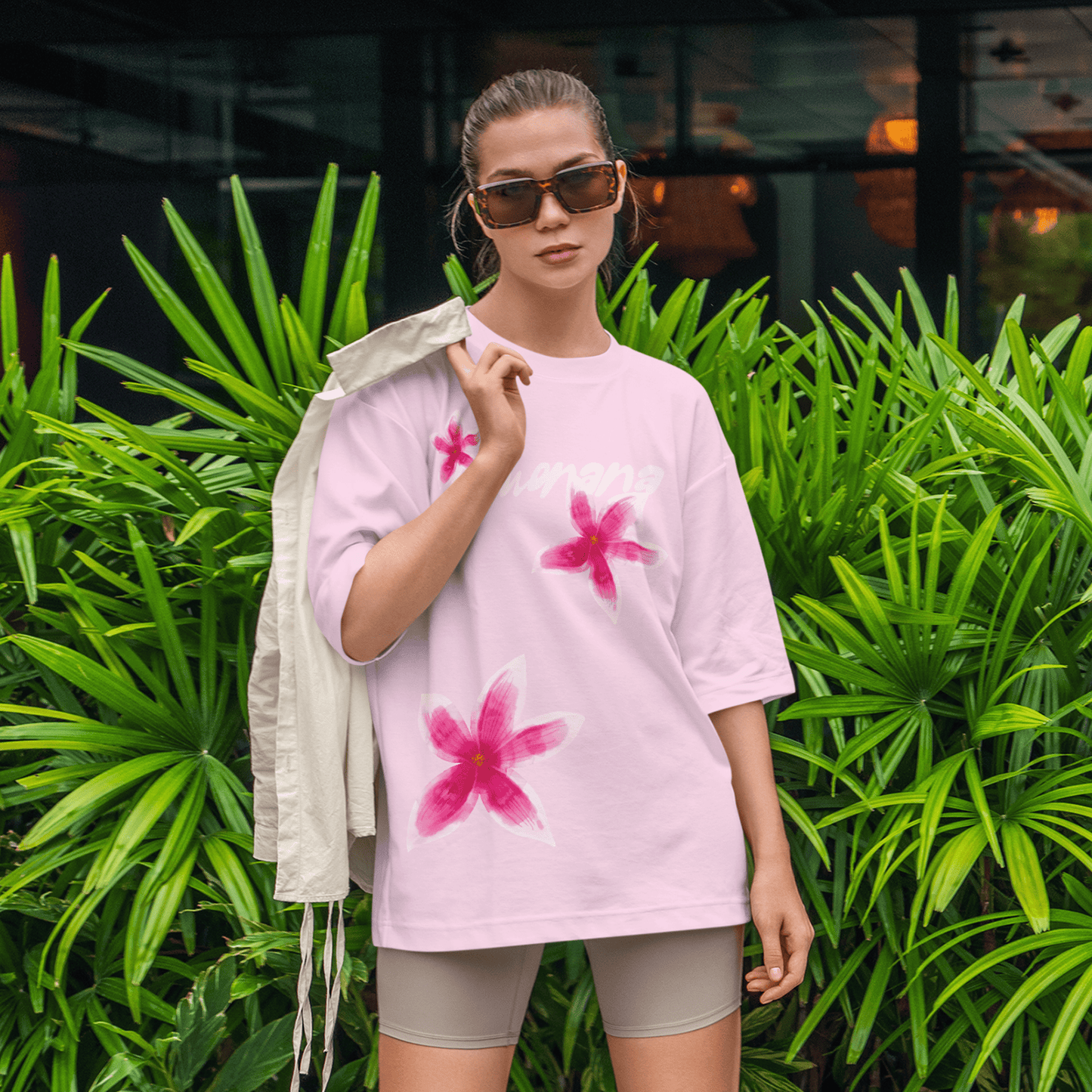 Woman wearing a pink t-shirt with floral designs in front of green plants