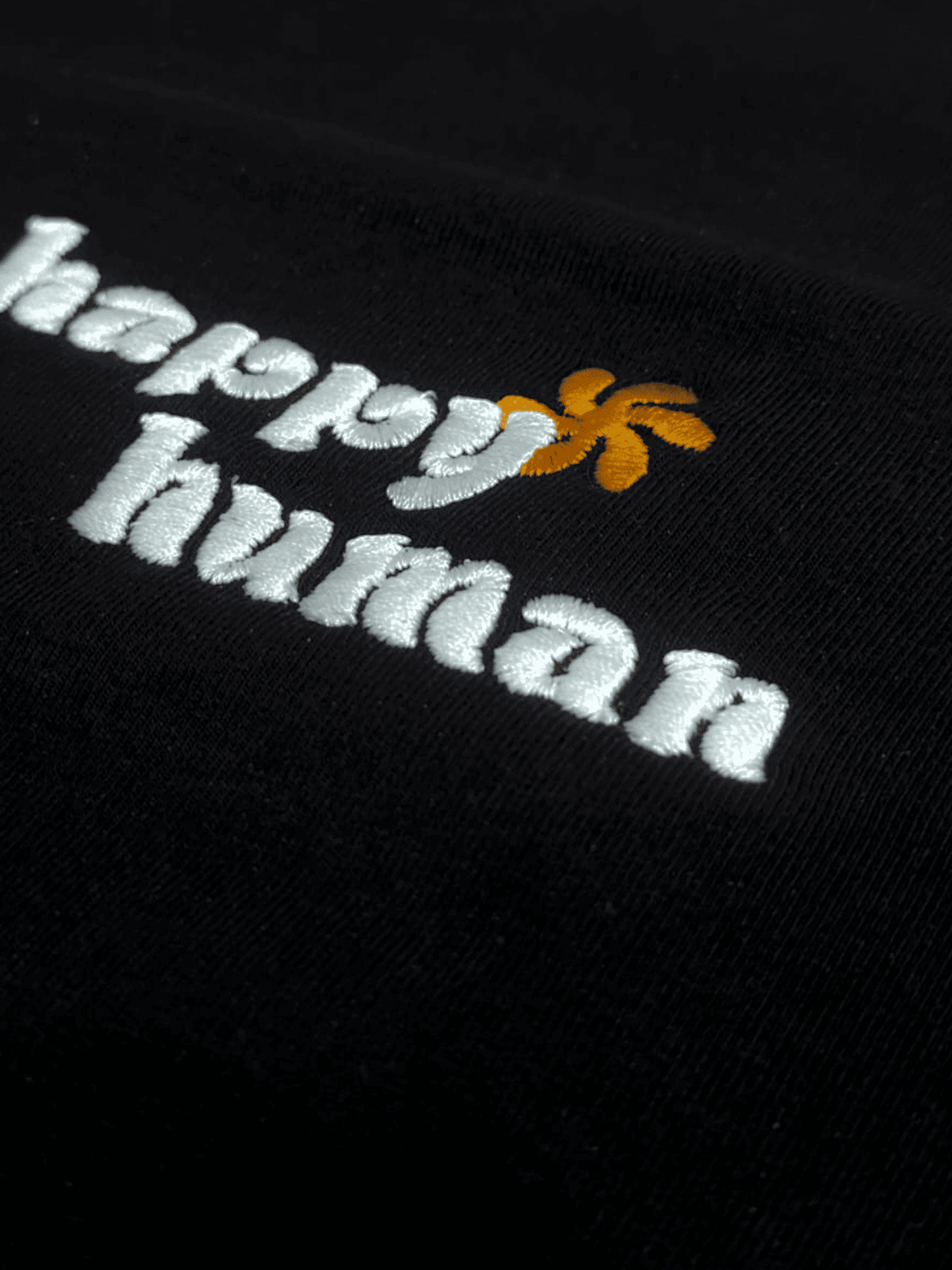 Embroidered 'happy human' text with a small floral design on a black background